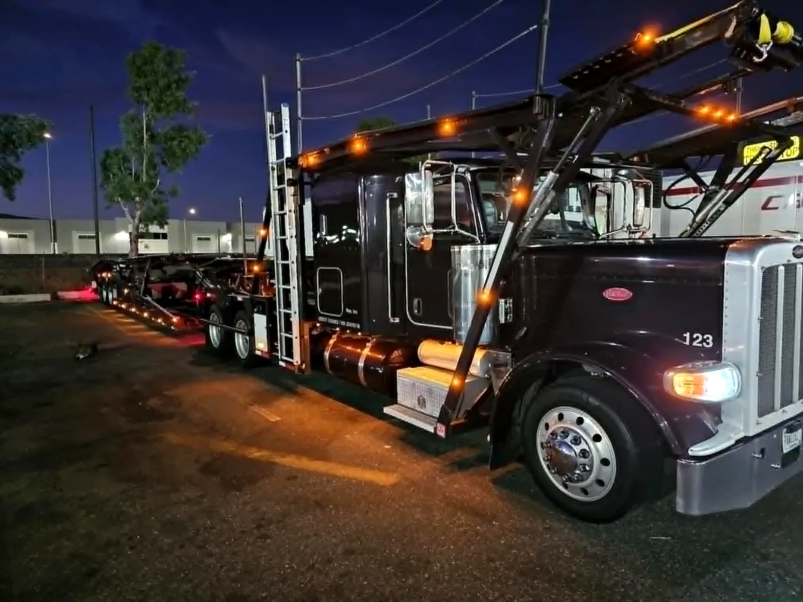 Car-hauling tractor and adjustable carrier structure illuminated at night.