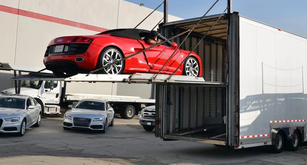Red Audi sports car on a platform being loaded into an enclosed trailer.