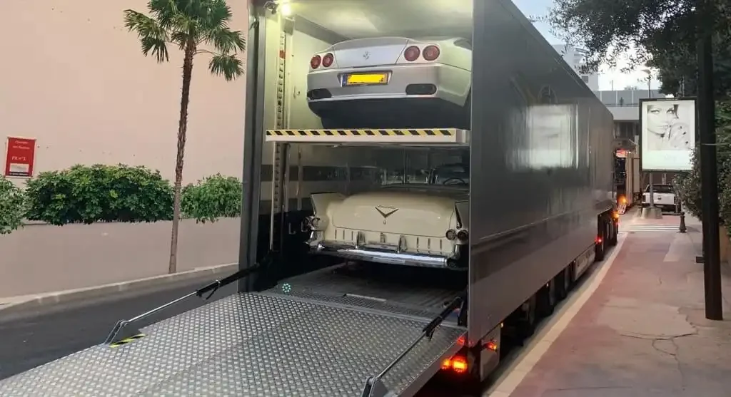 Two classic vehicles inside a two-level enclosed transport trailer with ramp lowered.