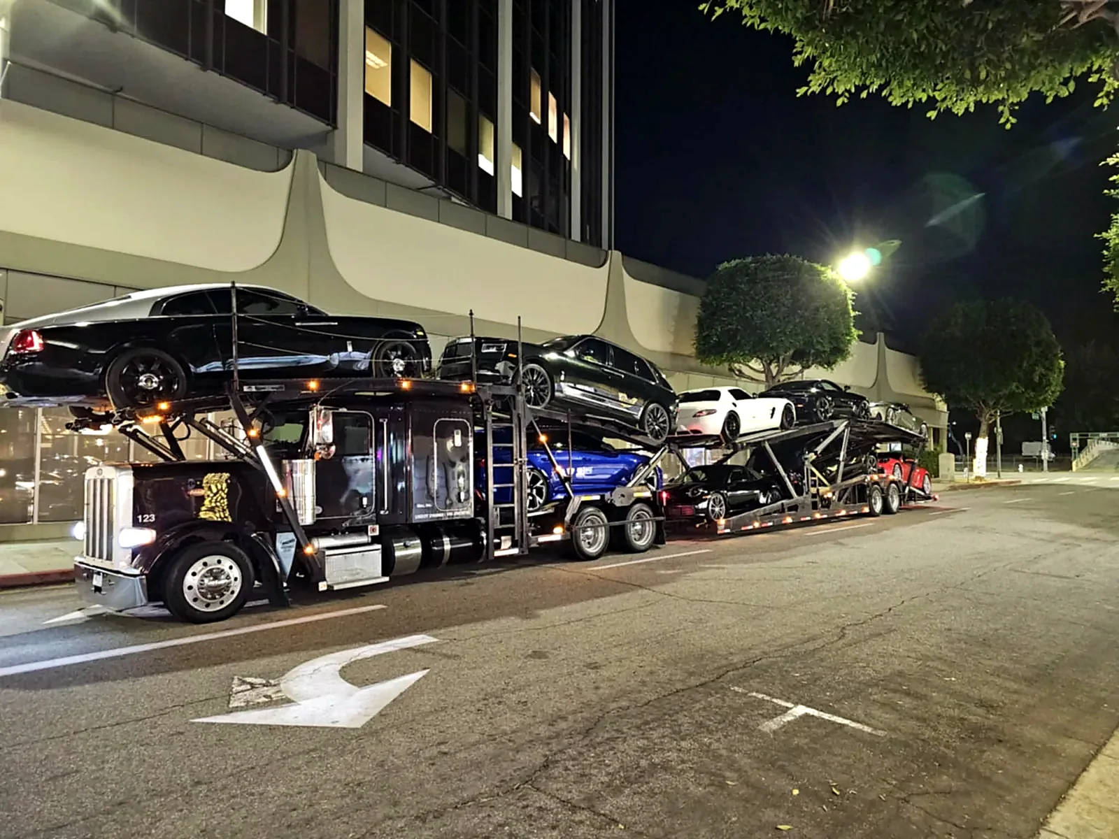 Loaded multi-car transporter parked beside a building at night.